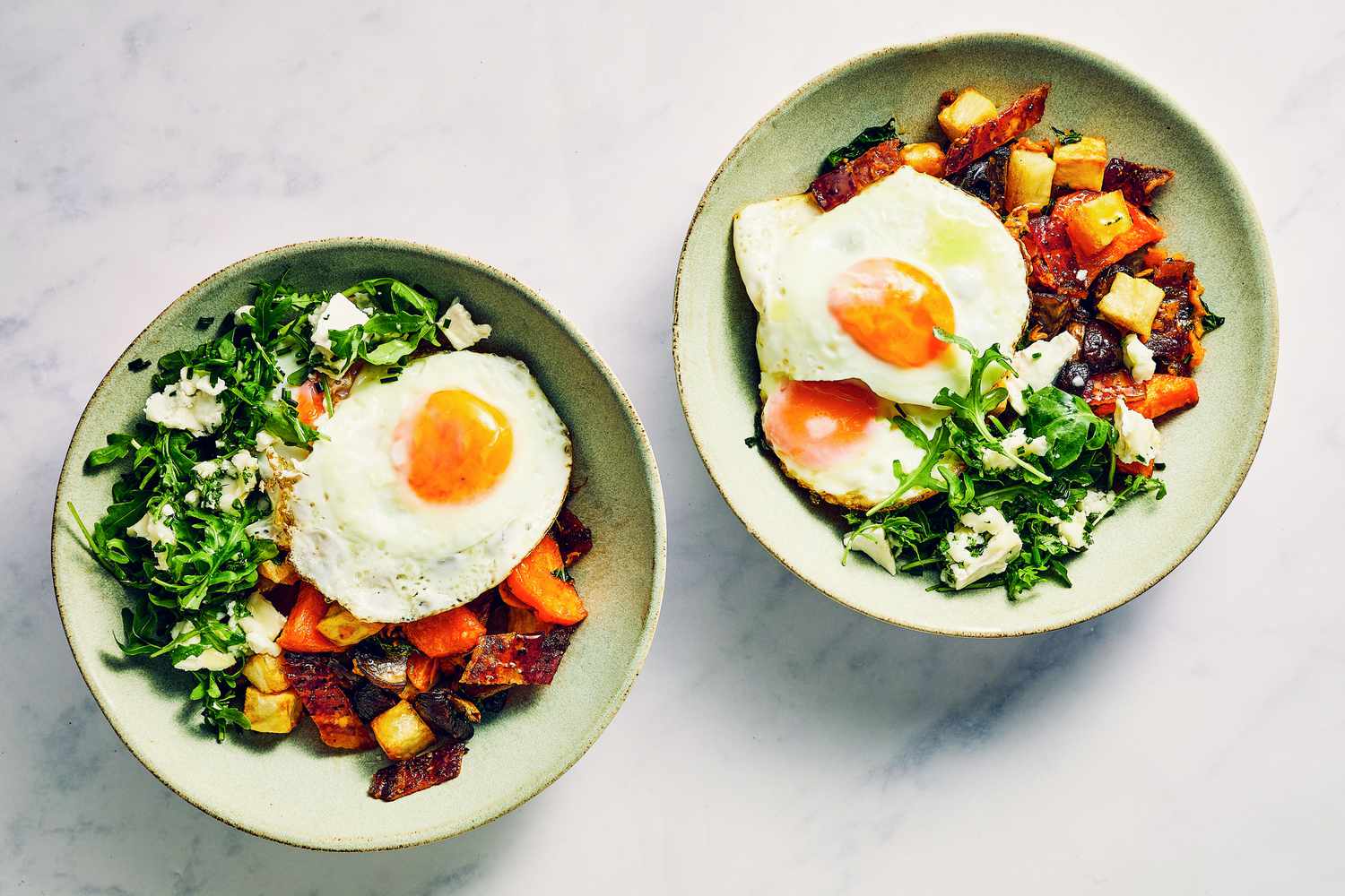 Two bowls of breakfast potato-mushroom hash, topped with arugula salad, and fried eggs