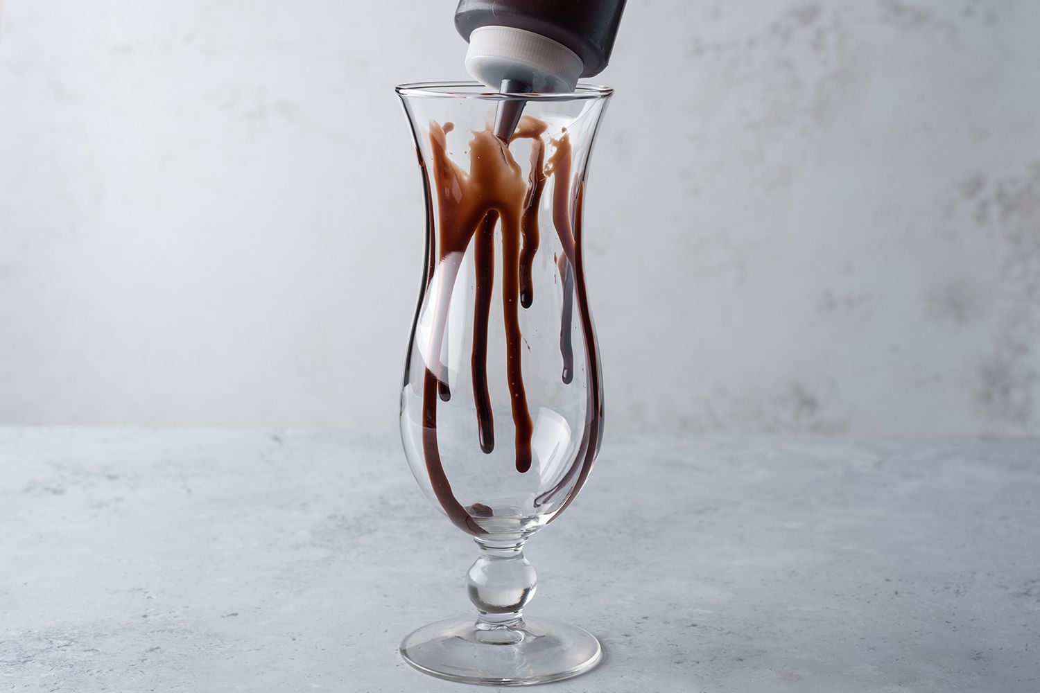 Drizzle chocolate syrup inside a hurricane glass