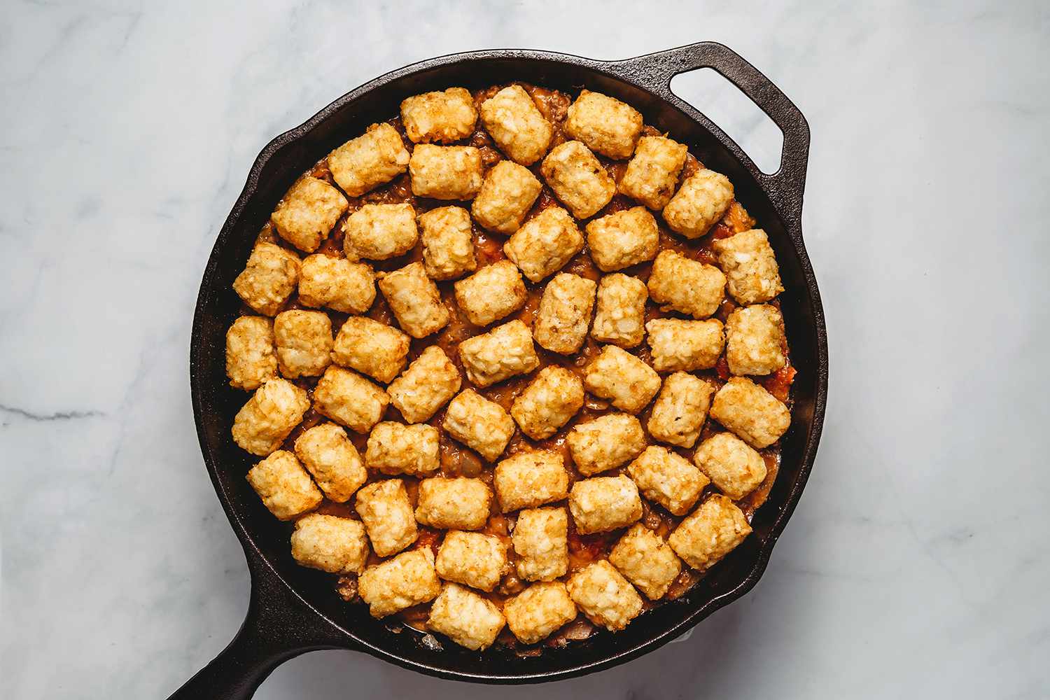 Tater tots on top of the beef mixture in the cast iron pan 
