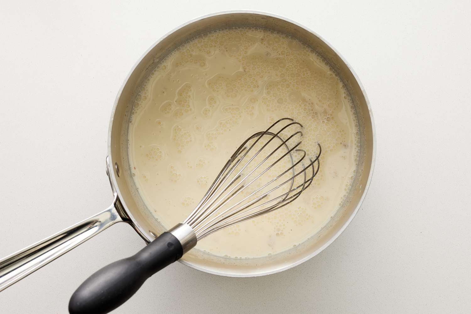 A whisk mixing bloomed gelatin into the pot with warmed cream and sugar