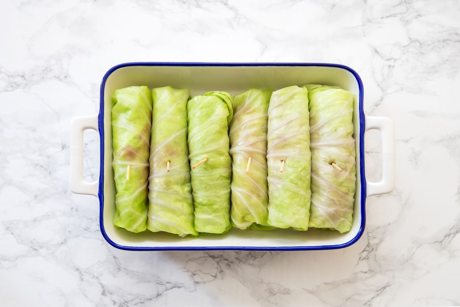 Cabbage rolls with a toothpick in a casserole pan on a white marble countertop