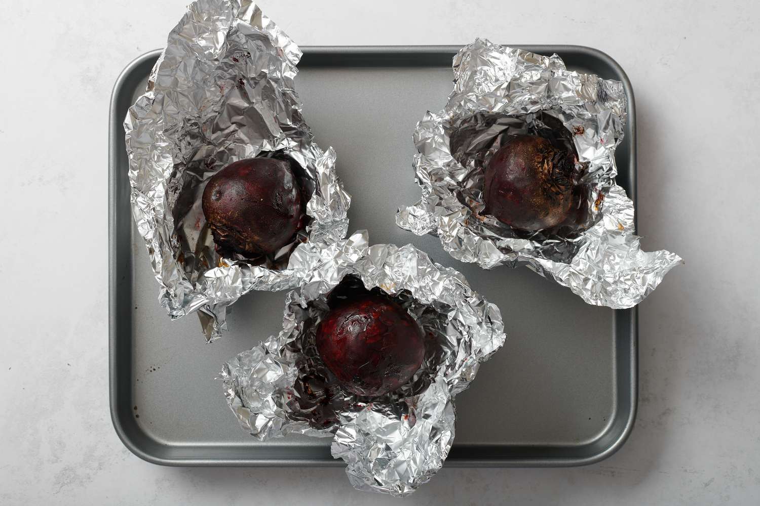 Baked beets wrapped in foil on a baking sheet