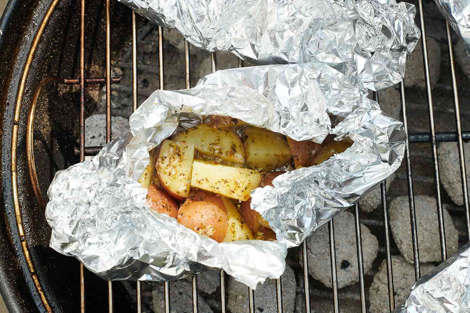 foil packets filled with potatoes on a charcoal grill