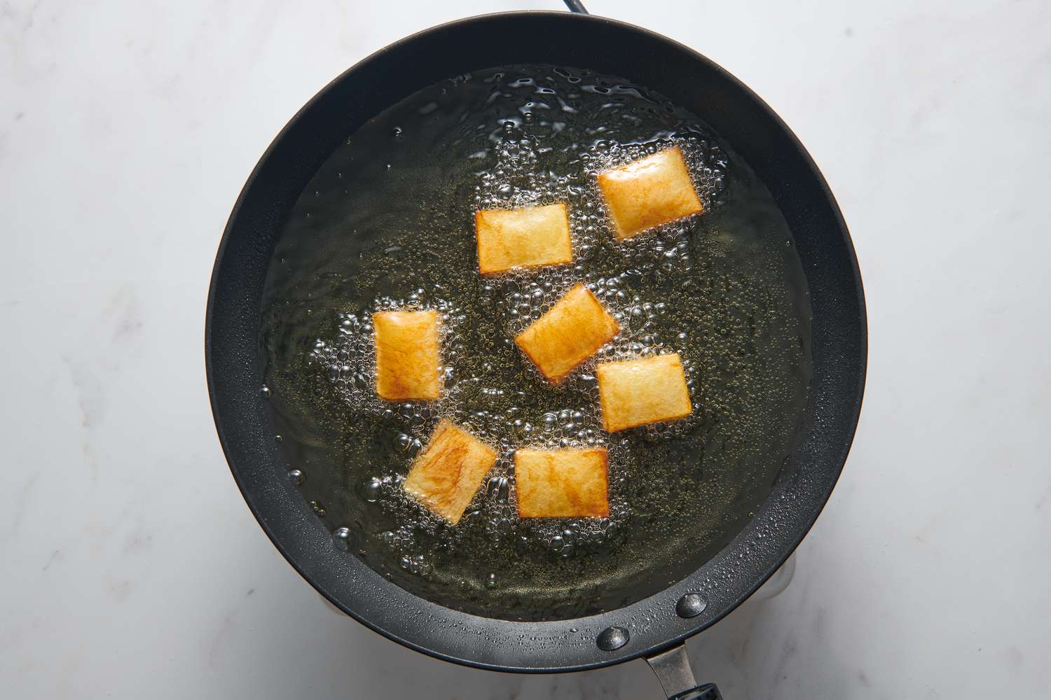 A large pan with small, golden brown rectangular stacks of thinly sliced potatoes frying in oil