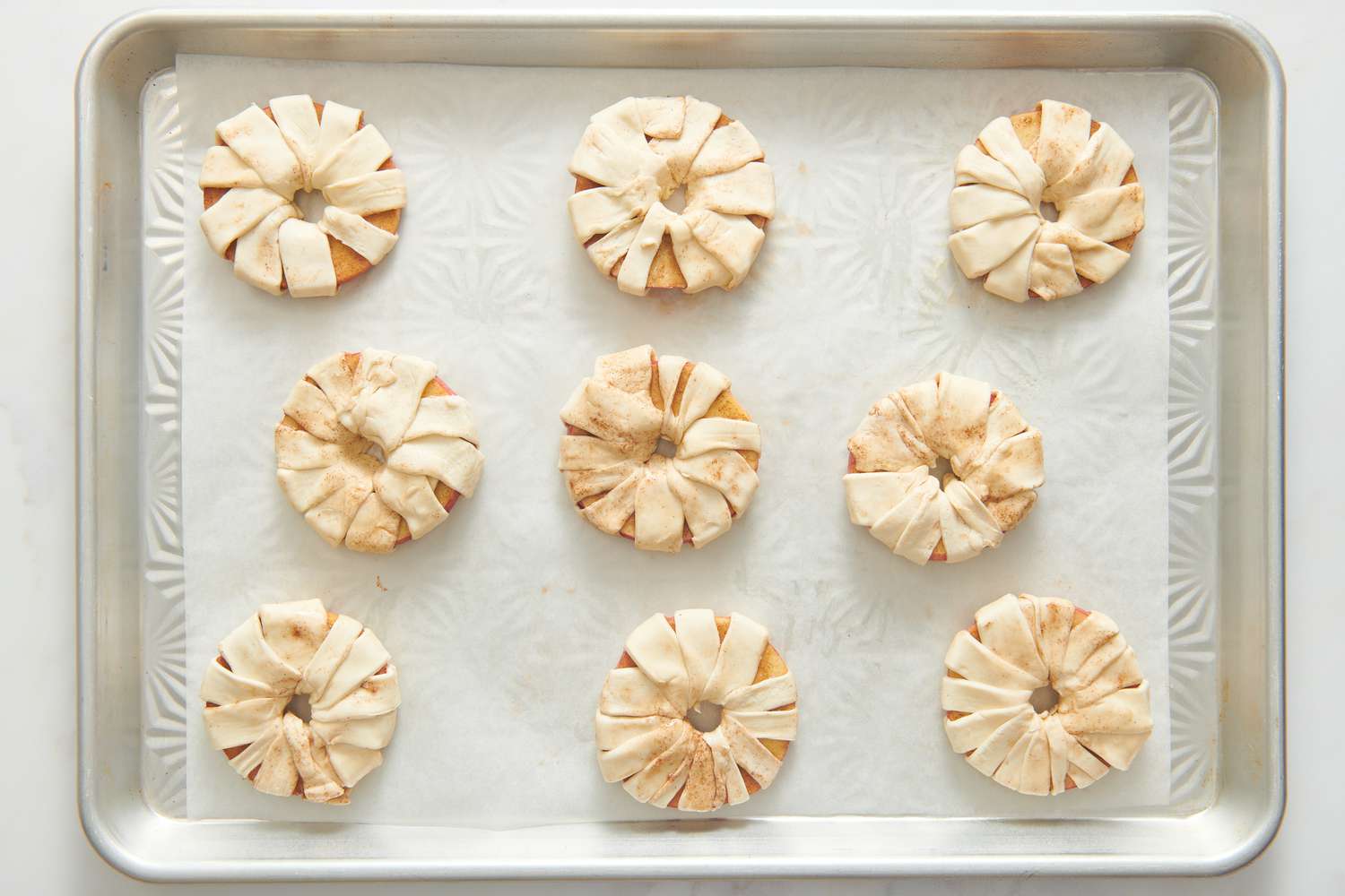 A parchment paper lined baking sheet with apple rings wrapped in strips of puff pastry