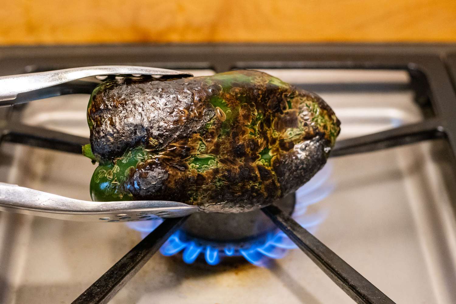Poblano pepper held with tongs over a gas burner 