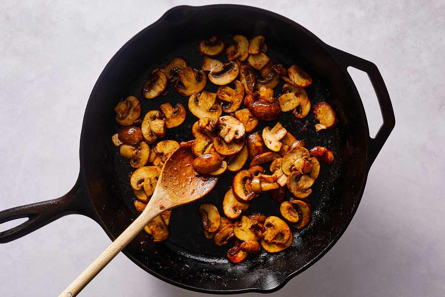 Mushrooms cooking in a cast iron skillet, with a wooden spoon 