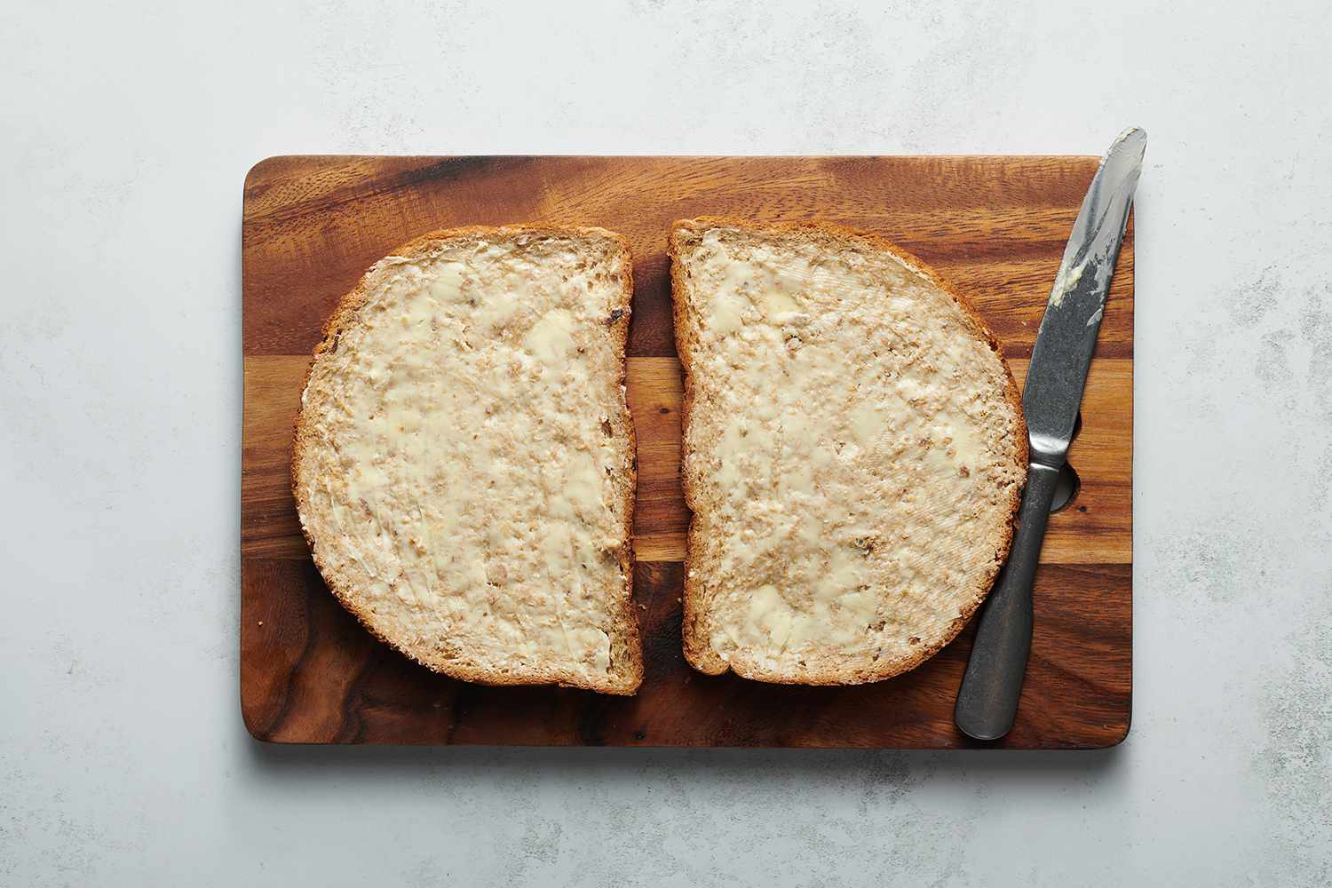 two slices of buttered bread on a wood cutting board