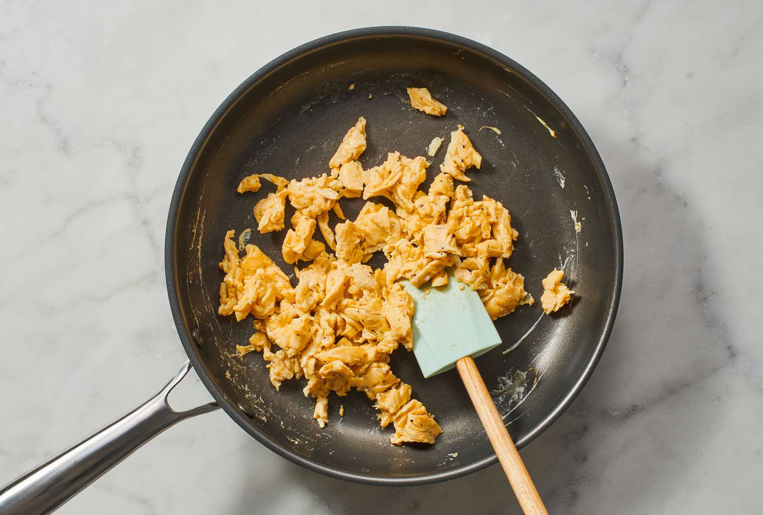 A rubber spatula tossing scrambled eggs in a pan