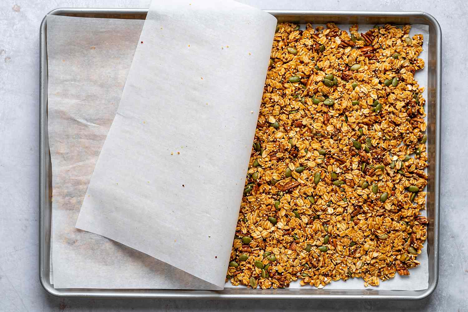 granola on a parchment lined baking sheet covered with parchment paper