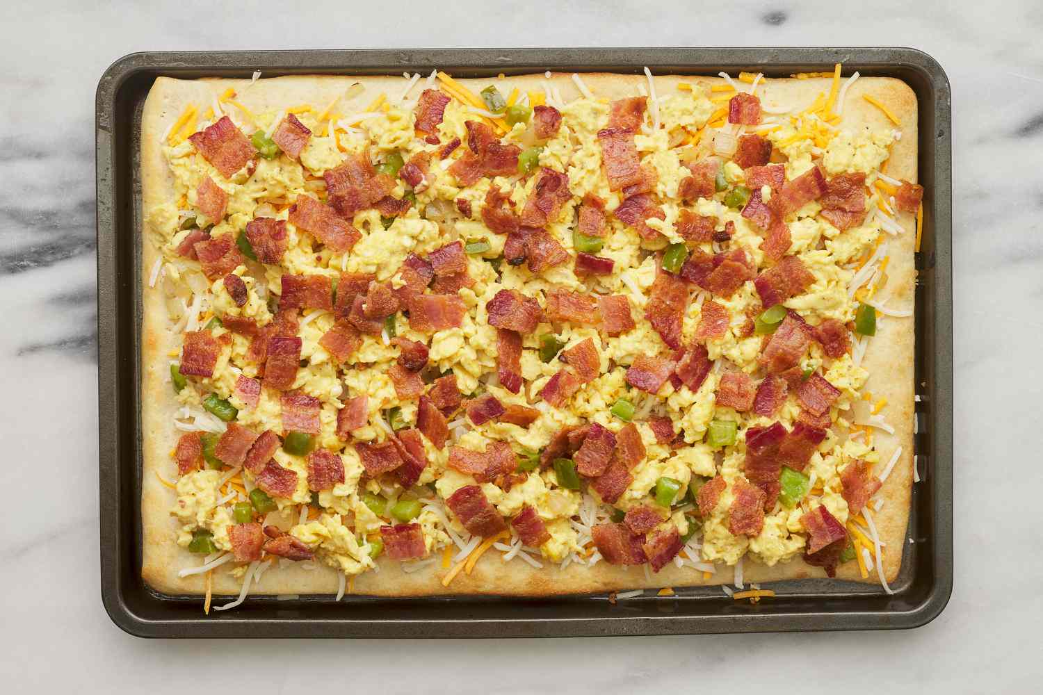 eggs, peppers, onion, cheese and bacon on pre-baked pizza crust in sheet pan
