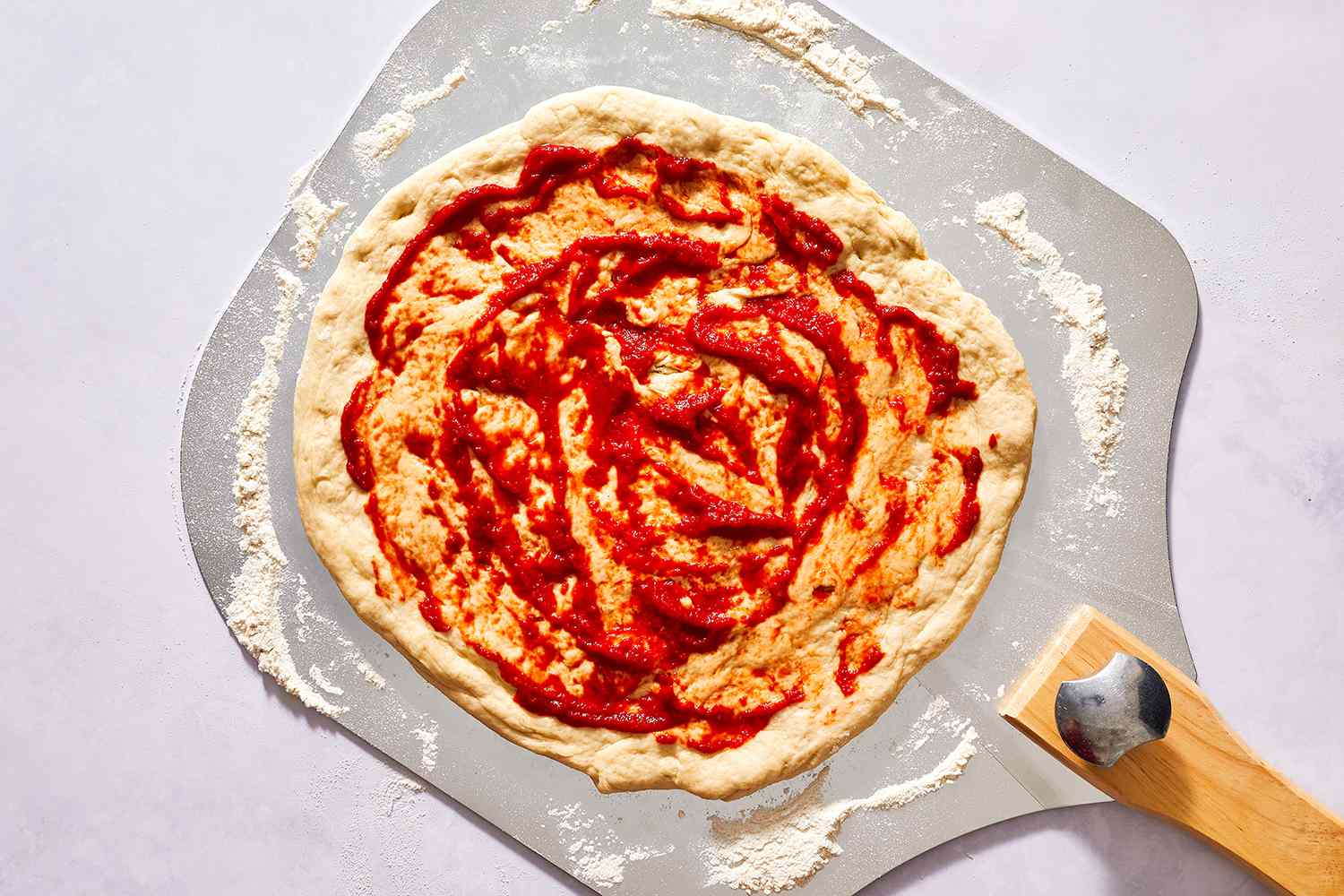 Pizza dough with tomato sauce spread to the edge, and set on a pizza peel