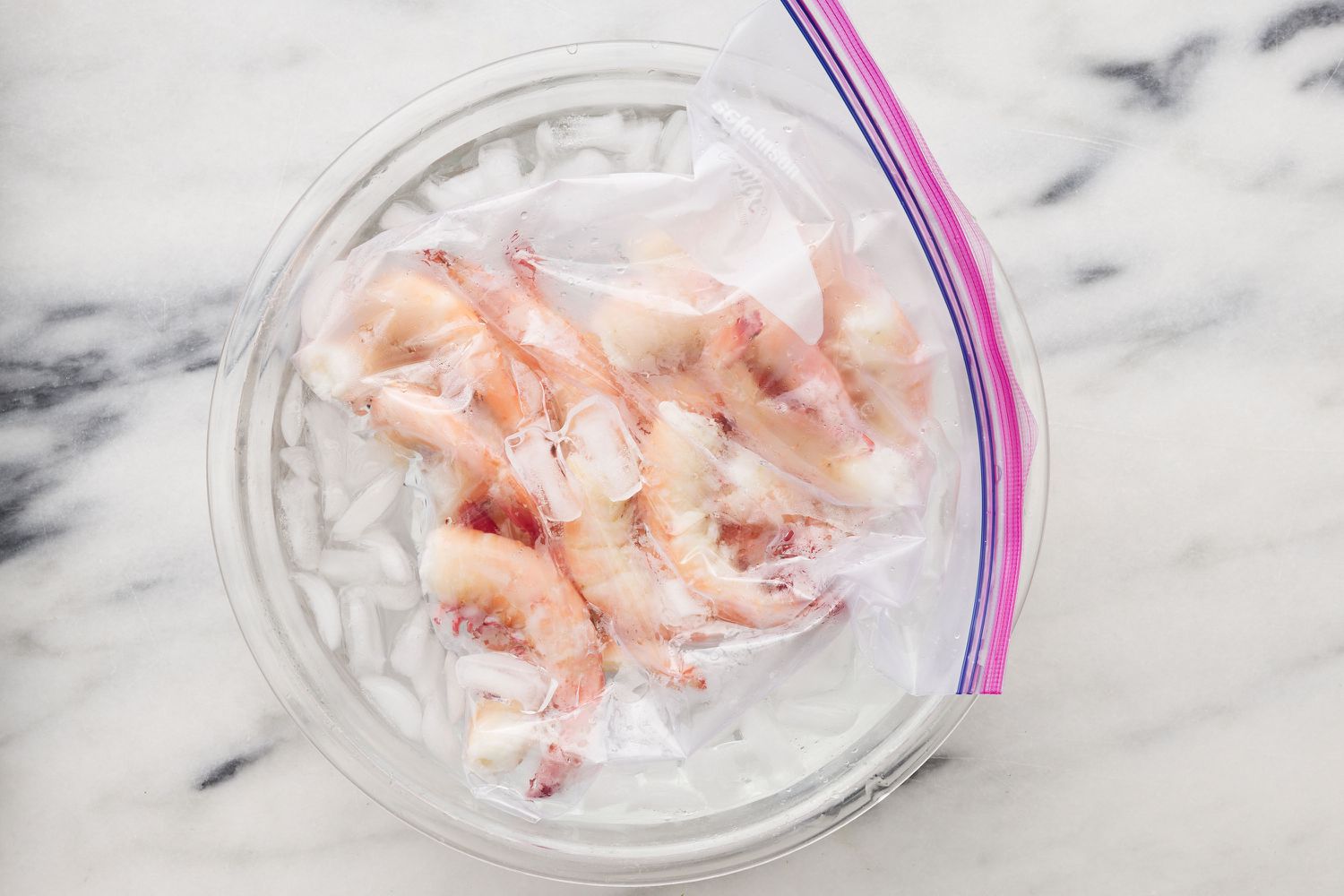 A lock top sealed plastic bag of poached shrimp sitting in a bowl of ice water