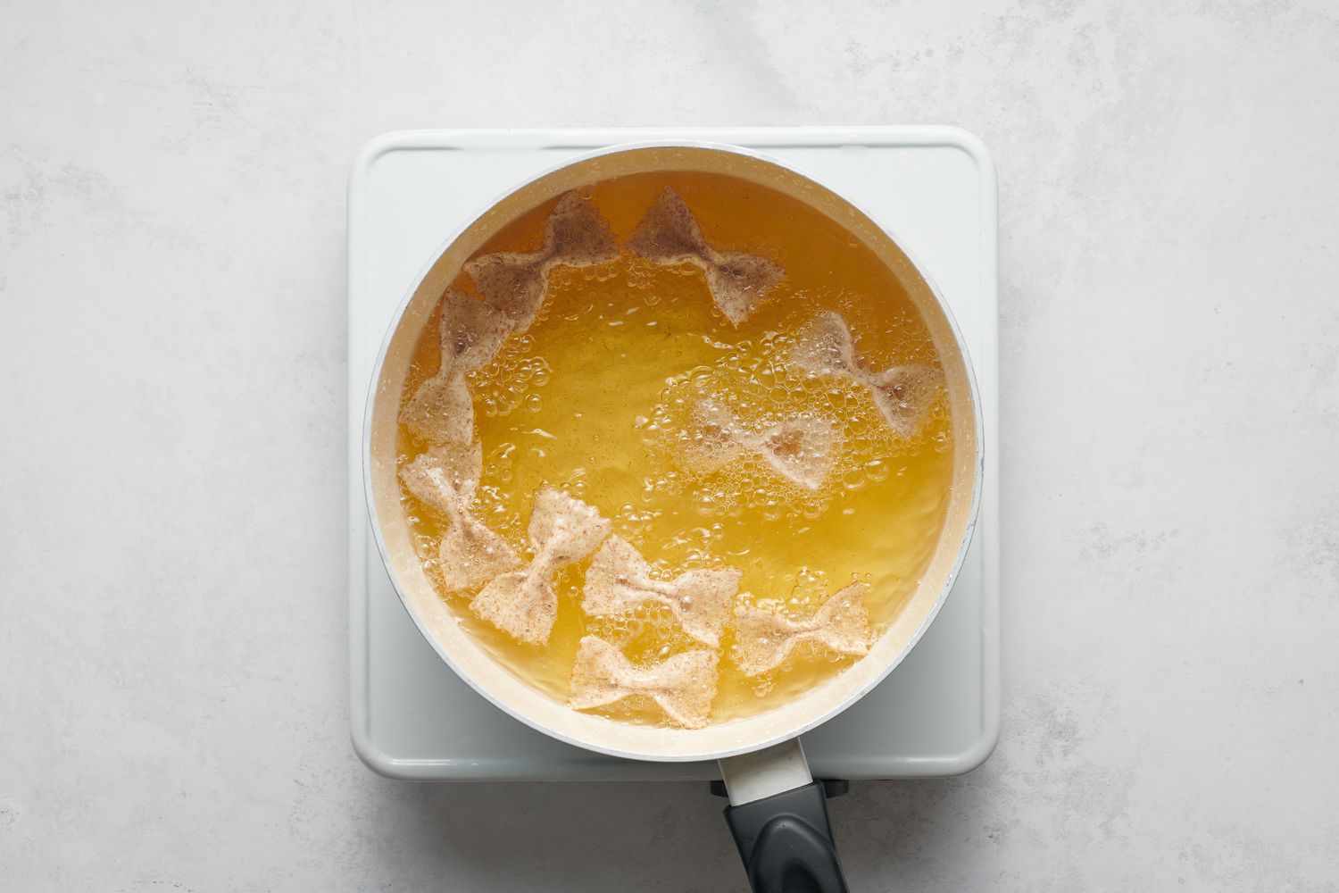 Pieces of bowtie-shaped pasta dough frying in a pot of oil