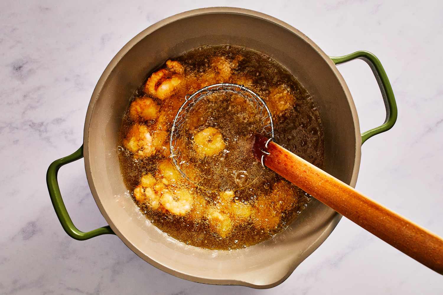 A spider strainer adding the coated shrimp into a pot of hot oil
