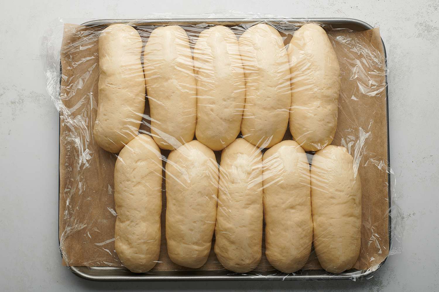 Dough logs on a parchment paper lined baking sheet, covered with plastic wrap 