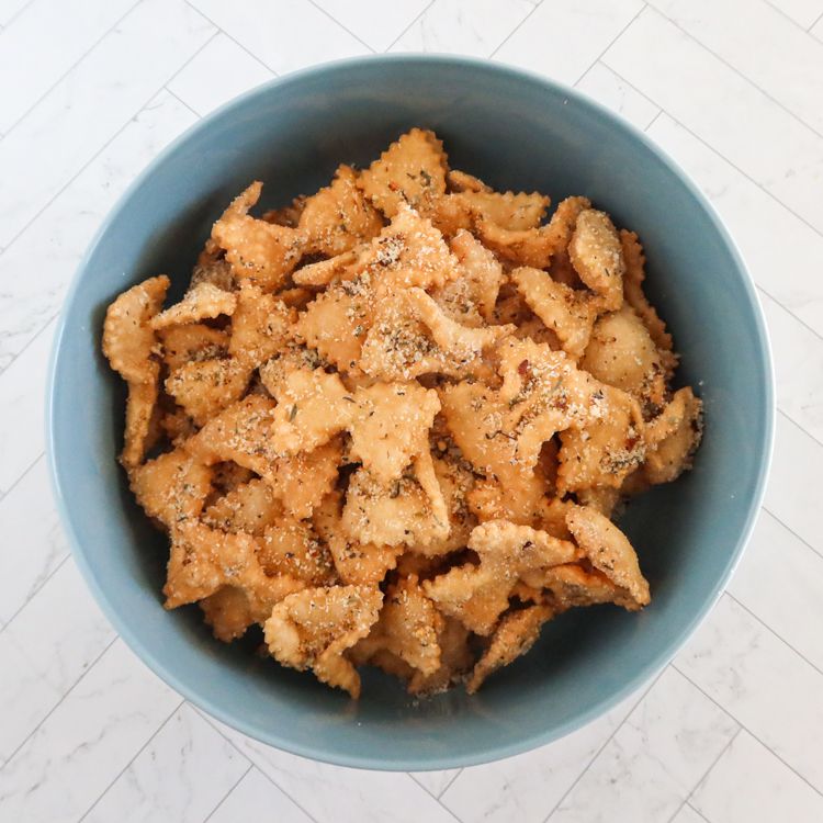 Golden brown fried farfalle (bowtie) pasta chips tossed with visible seasoning in a bowl