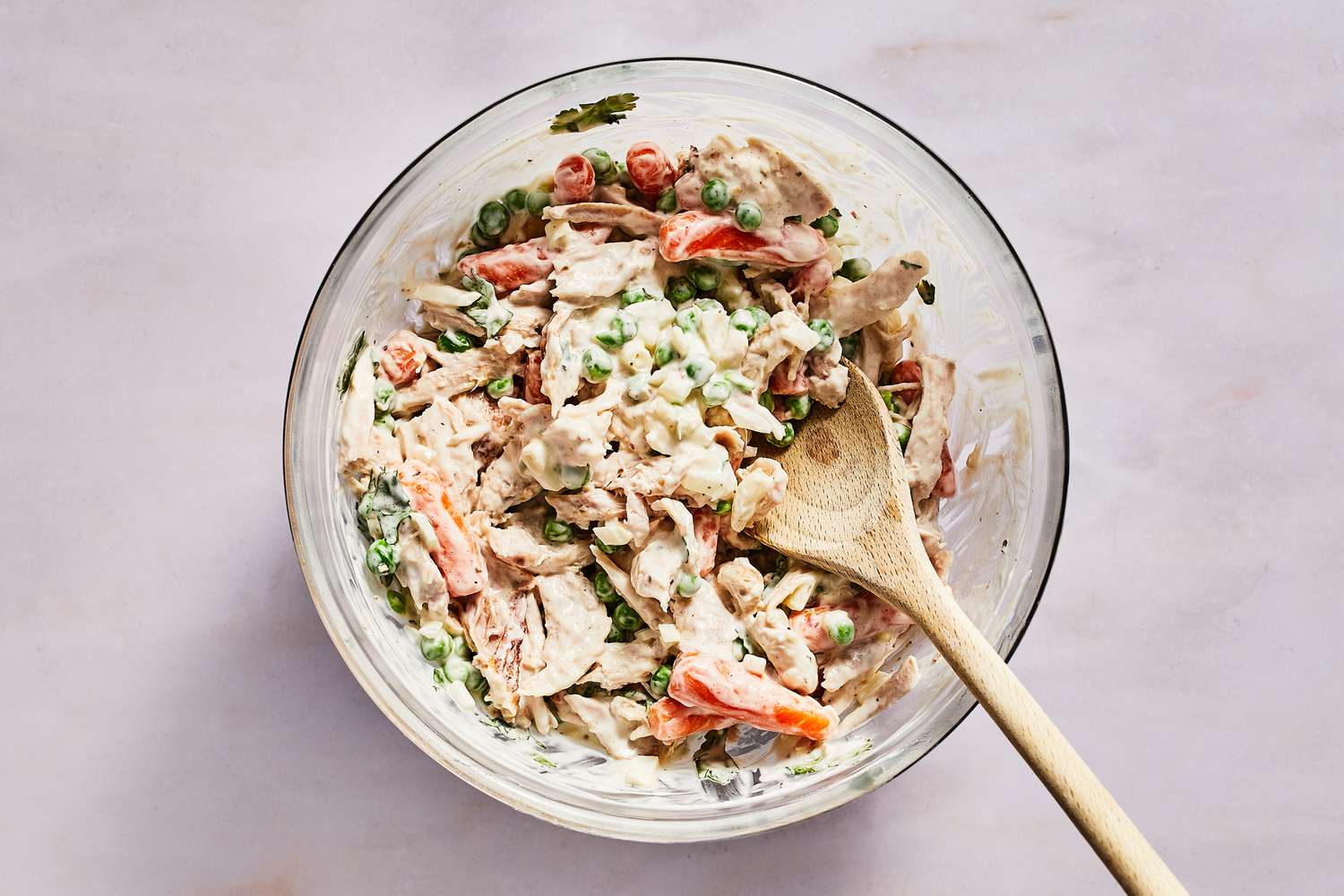 A bowl of shredded rotisserie chicken, peas, carrots, onion, and cilantro tossed in the mayonnaise-crema dressing