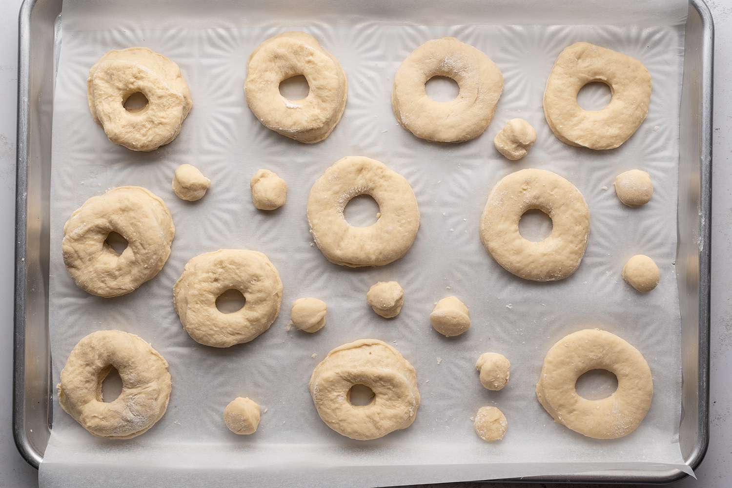 Doughnut dough shaped into doughnuts and doughnut holes on a prepared baking sheet
