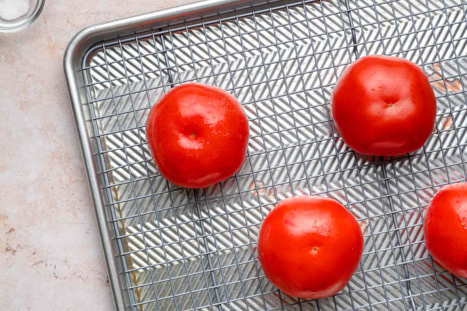 Four tomatoes, cut-side down on a baking rack over a baking sheet