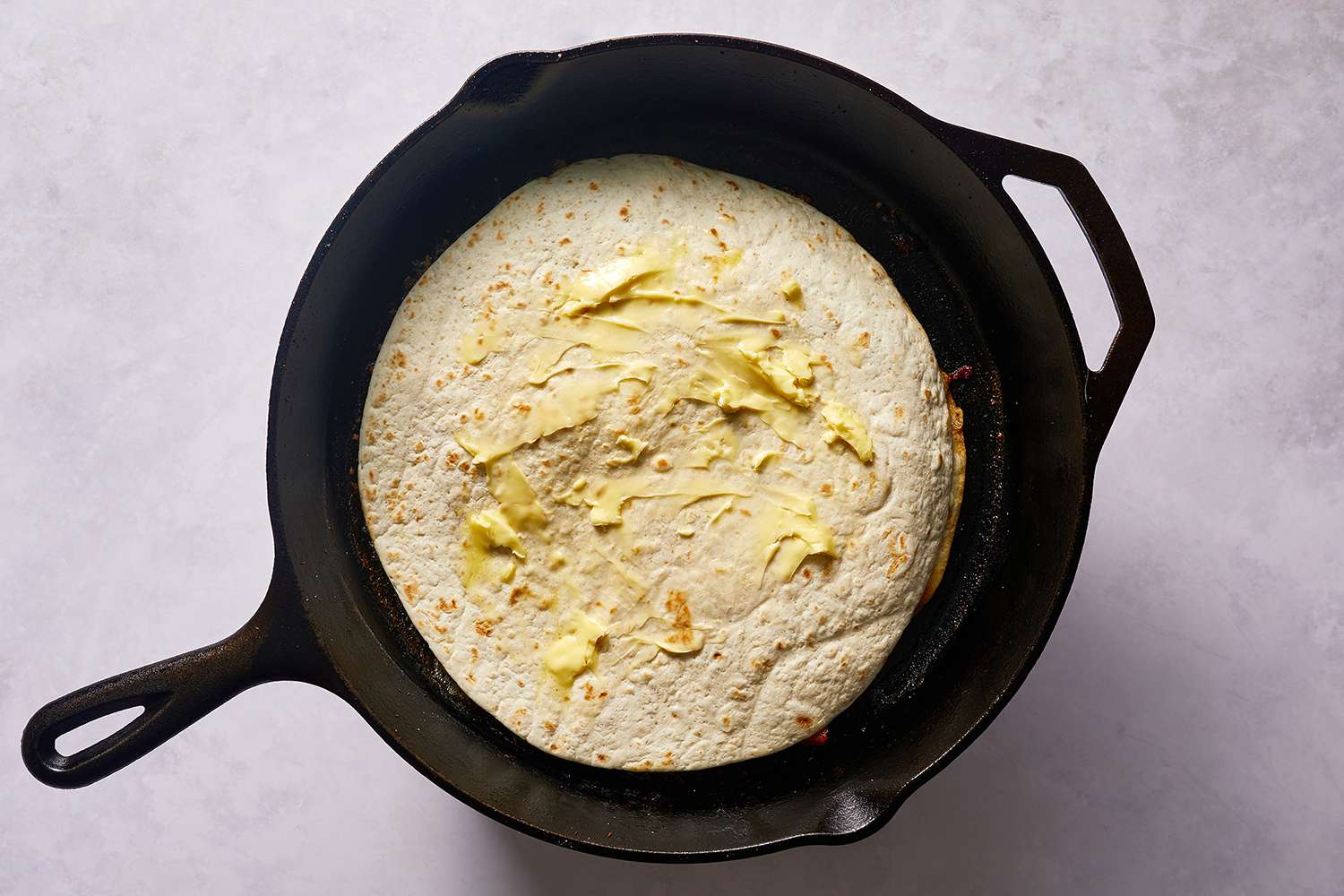 Quesadilla topped with another tortilla and butter, in a skillet 