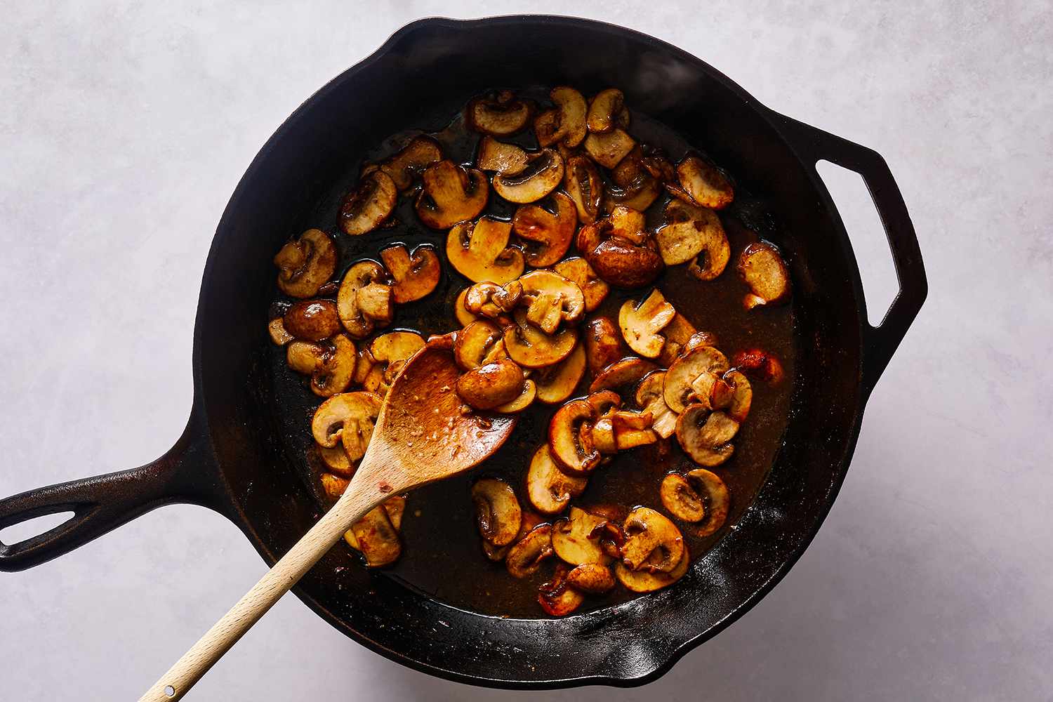 Mushrooms and sauce in a cast iron skillet, with a wooden spoon
