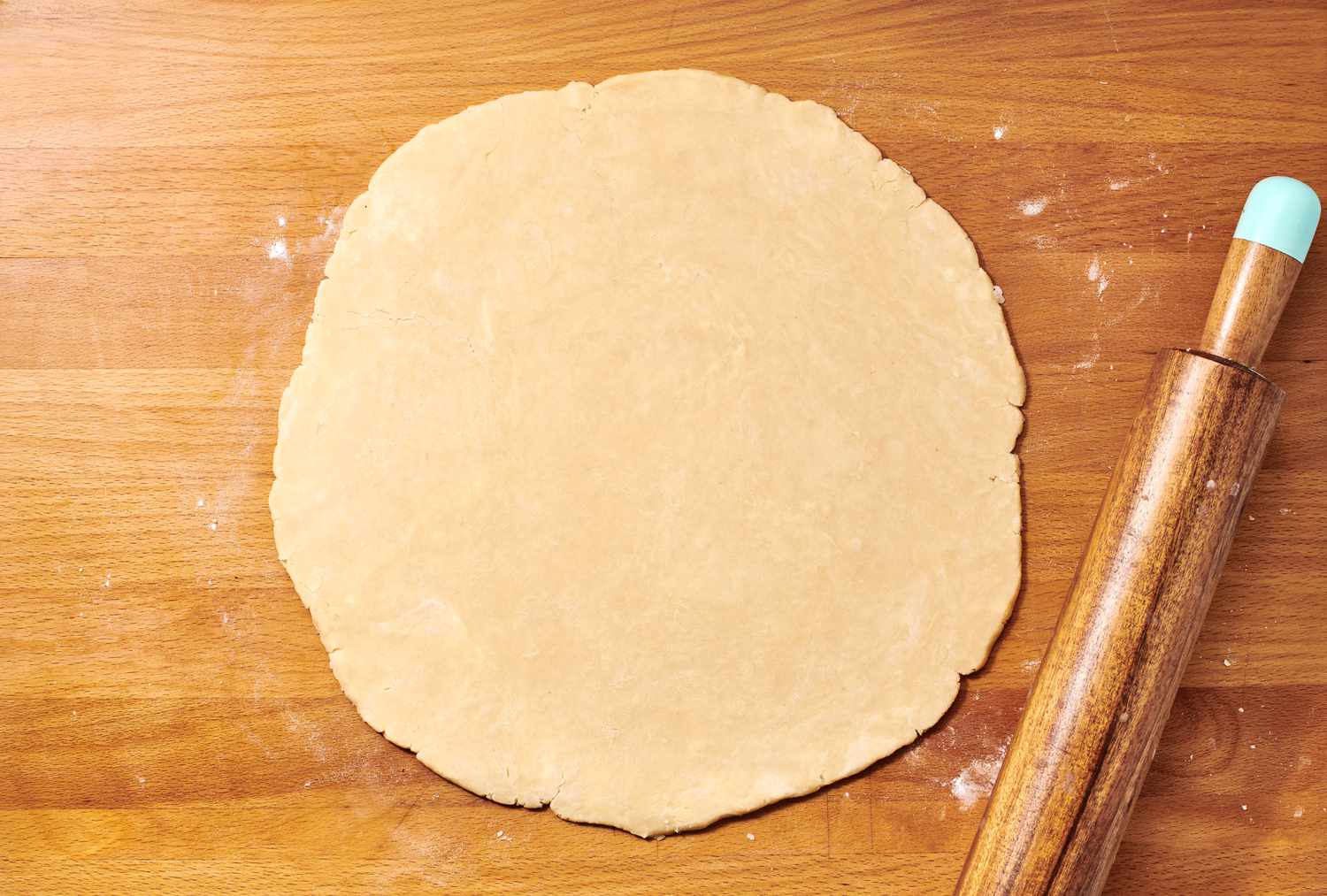 A large, flat round piece of dough on a floured surface with a rolling pin