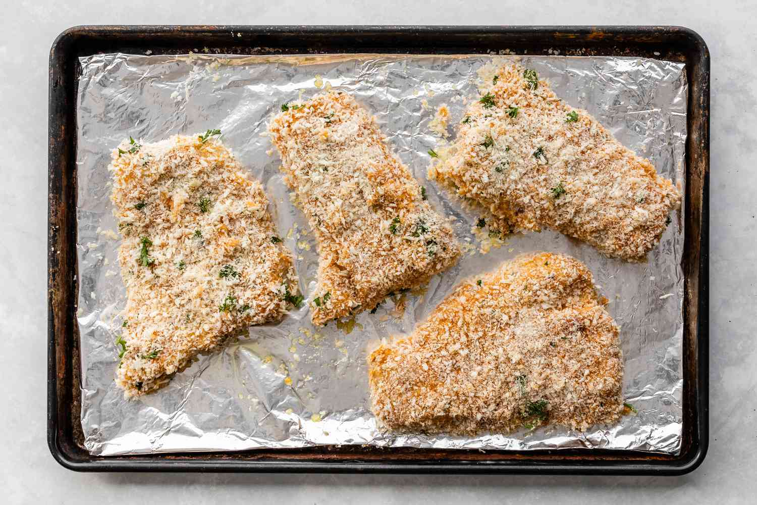 Panko-crusted haddock fillets on a rimmed baking sheet lined with foil