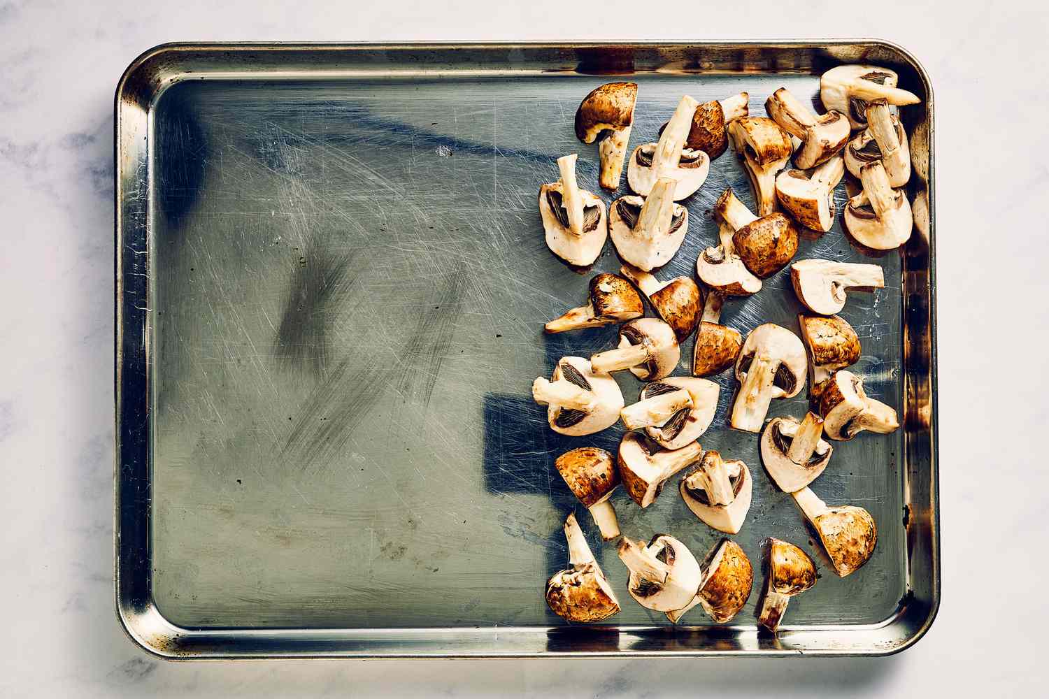 A sheet pan with half the pan covered in cremini mushrooms tossed in oil and seasoned with salt