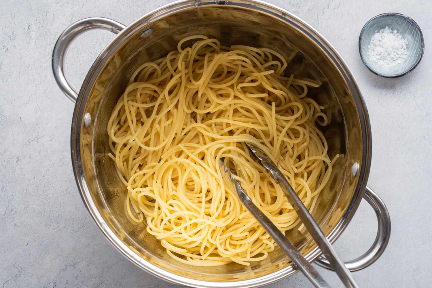 Cooked spaghetti in a pot with metal tongs