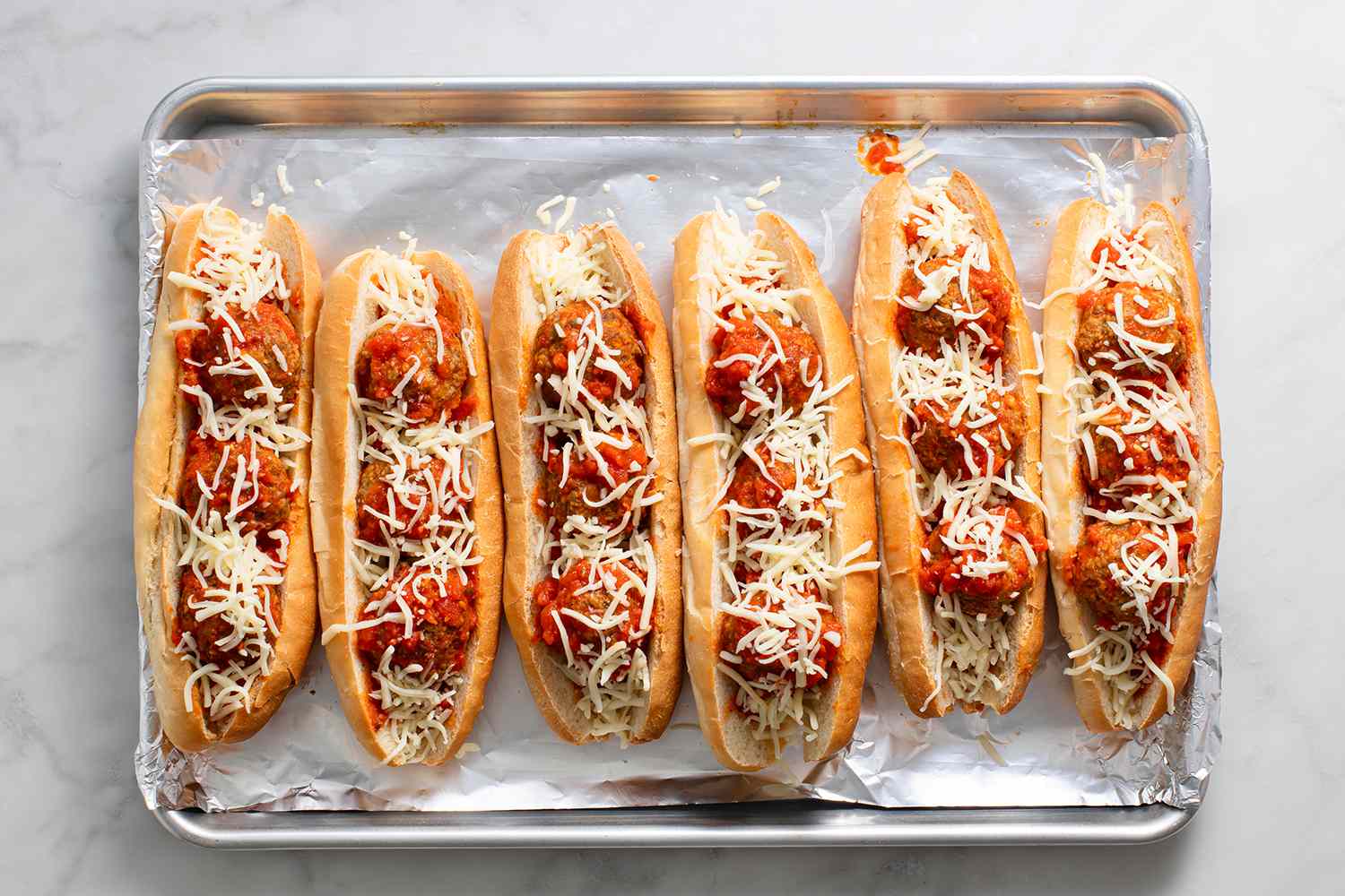 Meatball subs on a baking sheet topped with tomato sauce and cheese