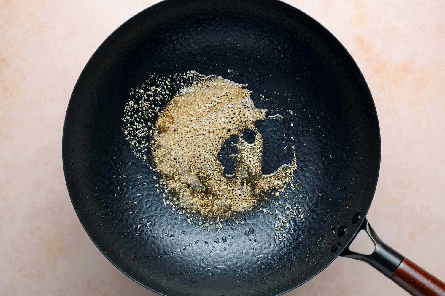 A large wok with sesame seeds, poppy seeds, and asafoetida frying in oil