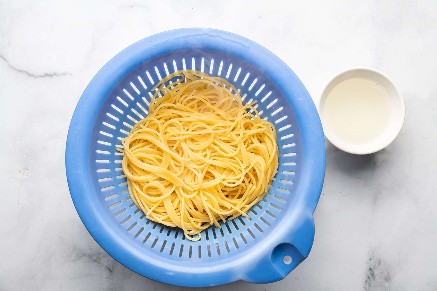 Pasta in a colander and pasta water in a bowl 