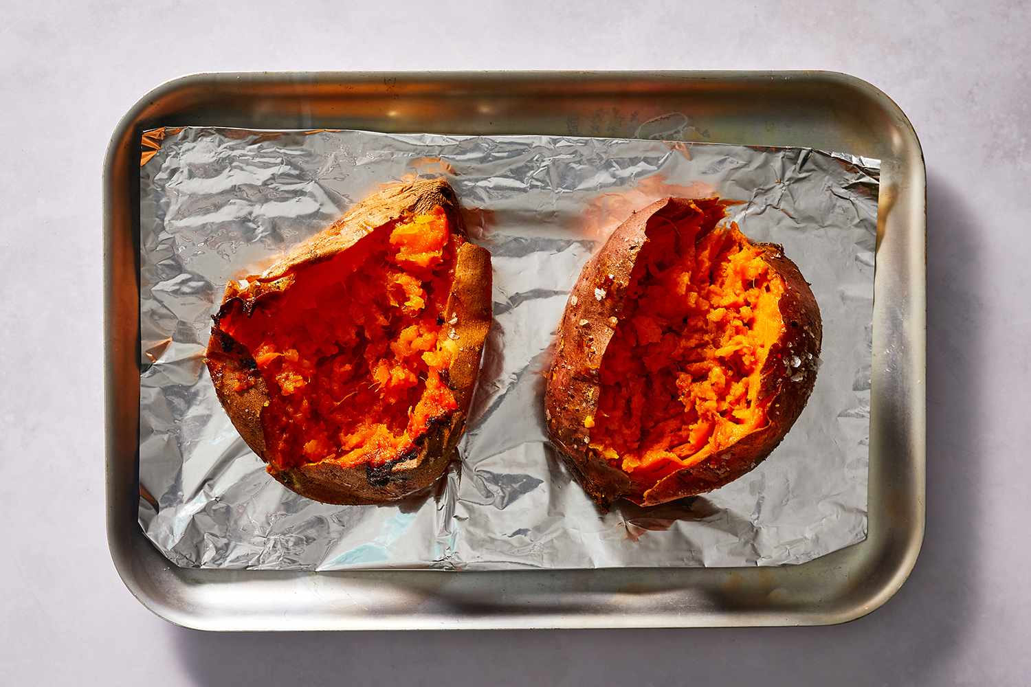Sweet potatoes split open on an aluminum foil lined baking sheet