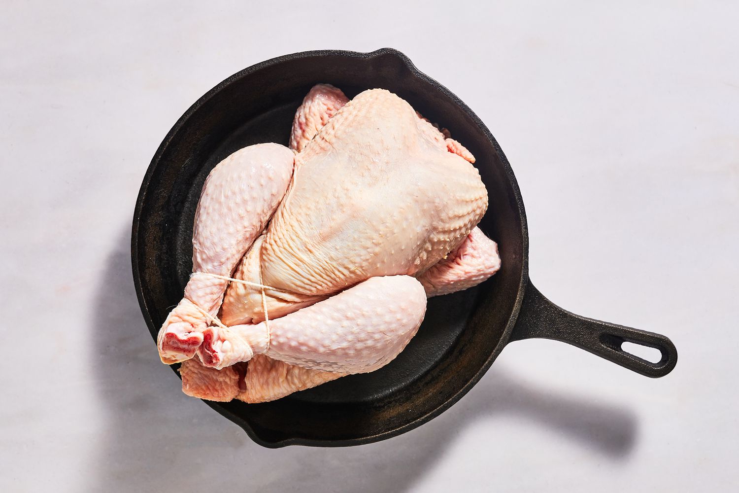 A trussed, whole chicken in a cast iron skillet