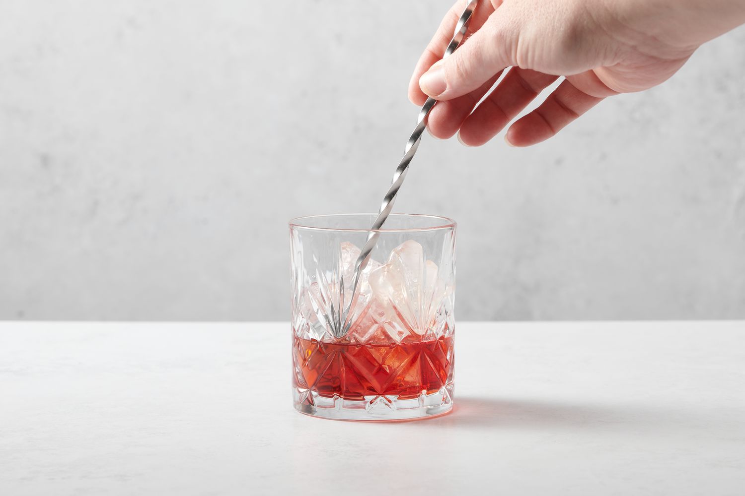 A hand stirring Campari and vermouth in a rocks glass with ice