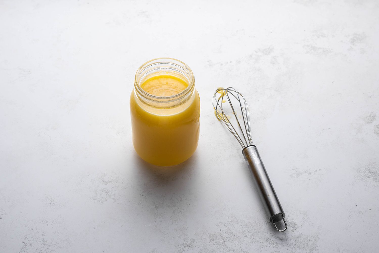 Lemon curd in a glass container, next to a whisk 