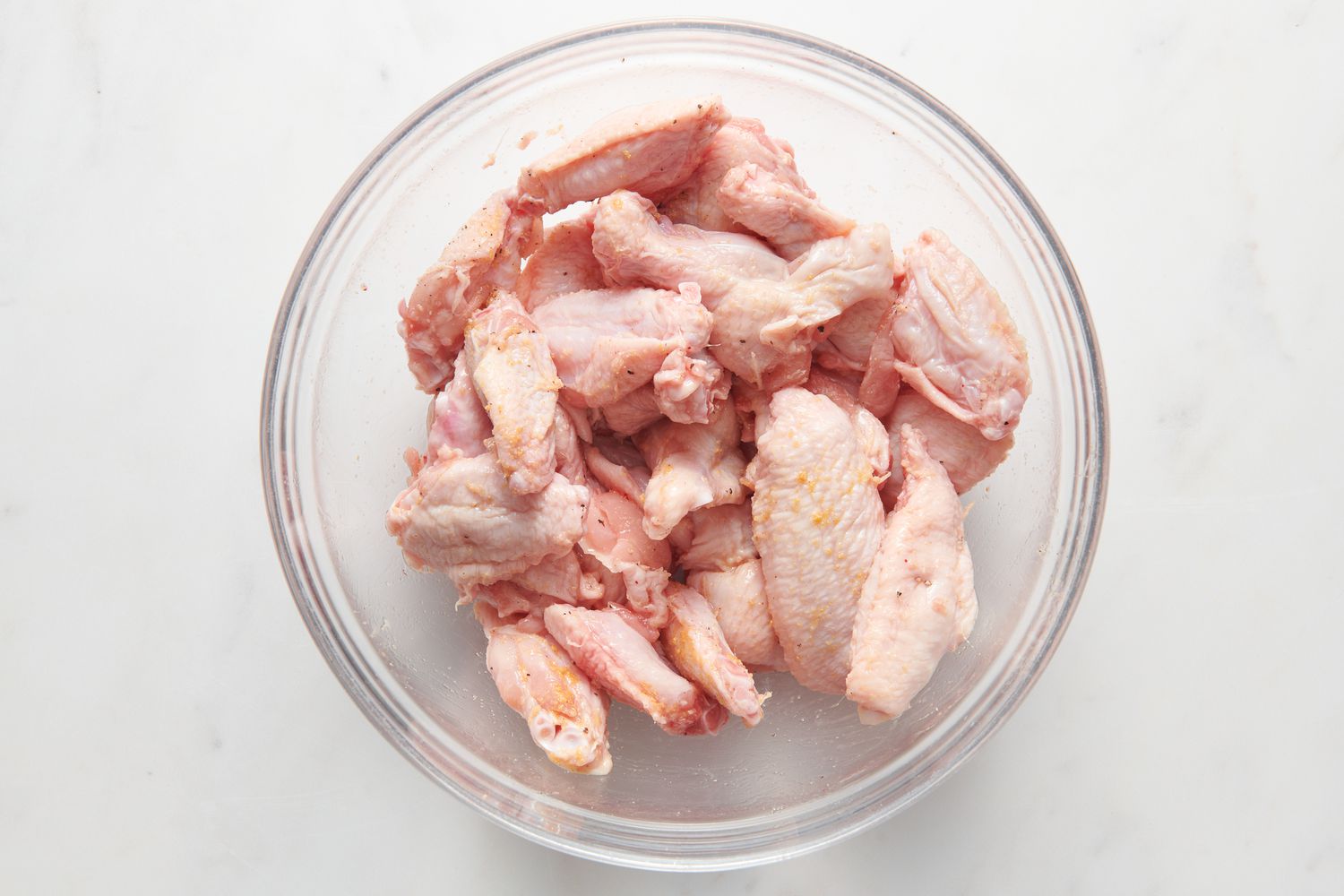 A large bowl of chicken wings coated with oil, salt, pepper, and garlic powder