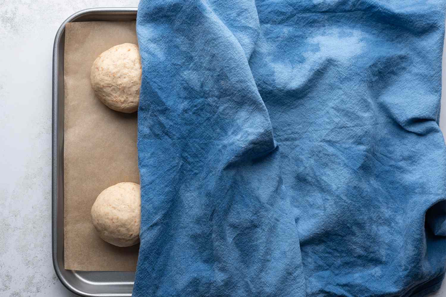 Dough balls on a parchment paper lined baking sheet, covered with a towel 