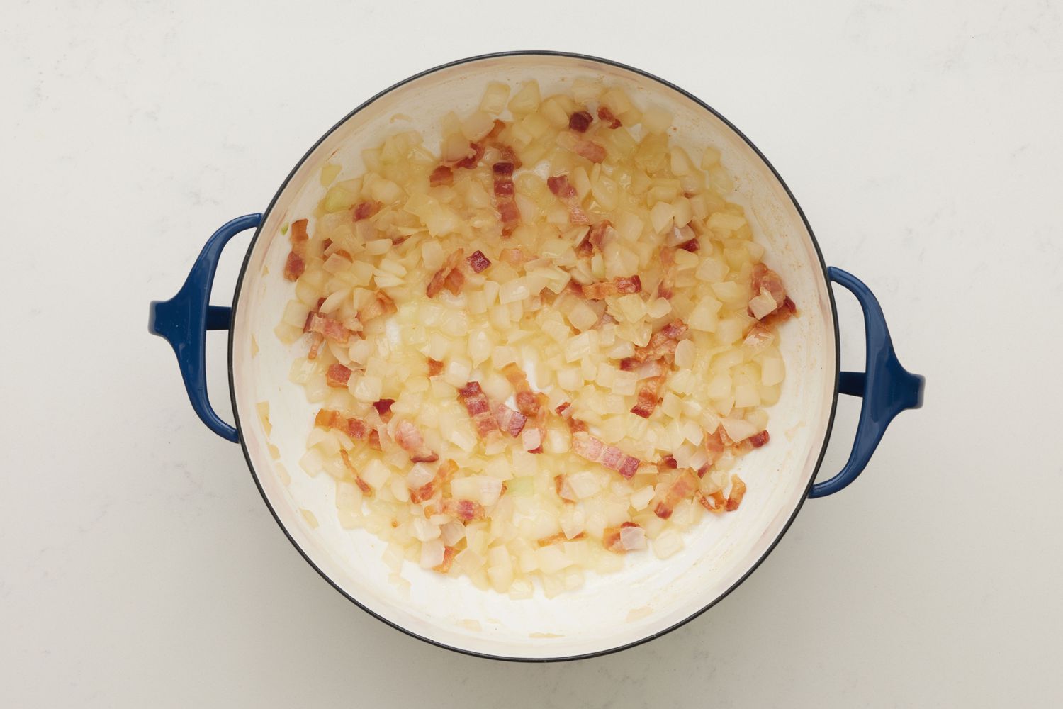 A dutch oven with cooked chopped bacon and diced onion, cooking down in butter and bacon fat