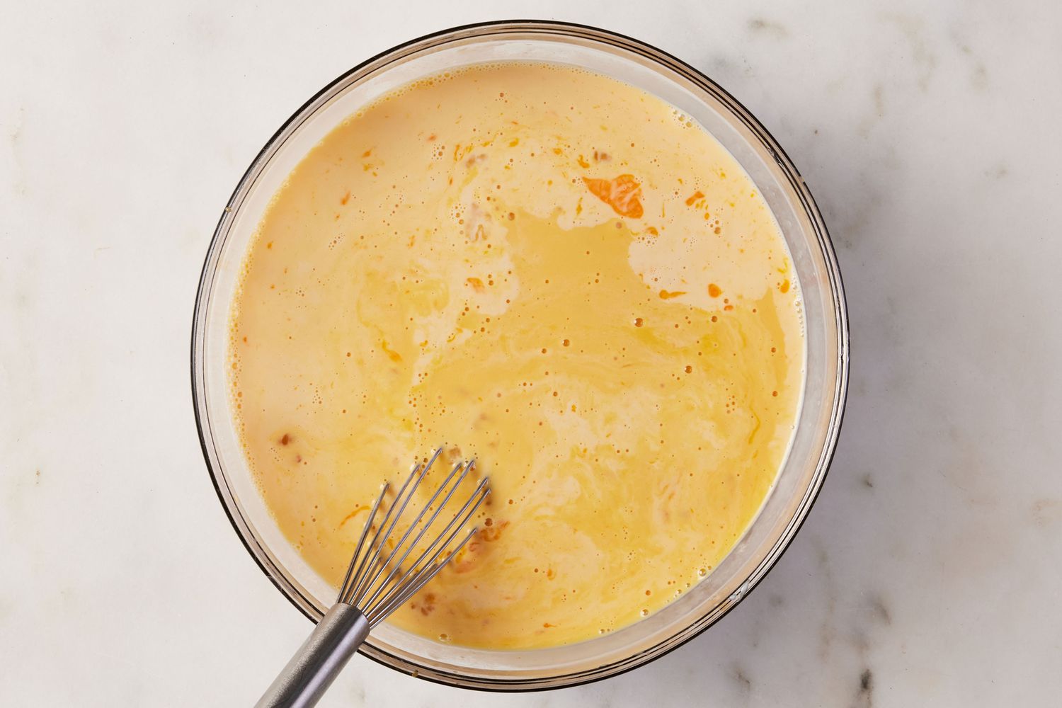 A large bowl of eggs, condensed milk, evaporated milk, and vanilla being whisked together