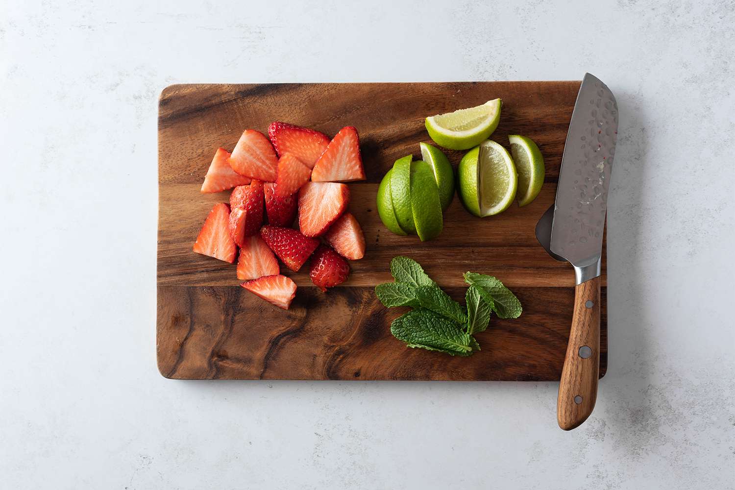 Cut strawberries, limes and mint on a cutting board with a knife 