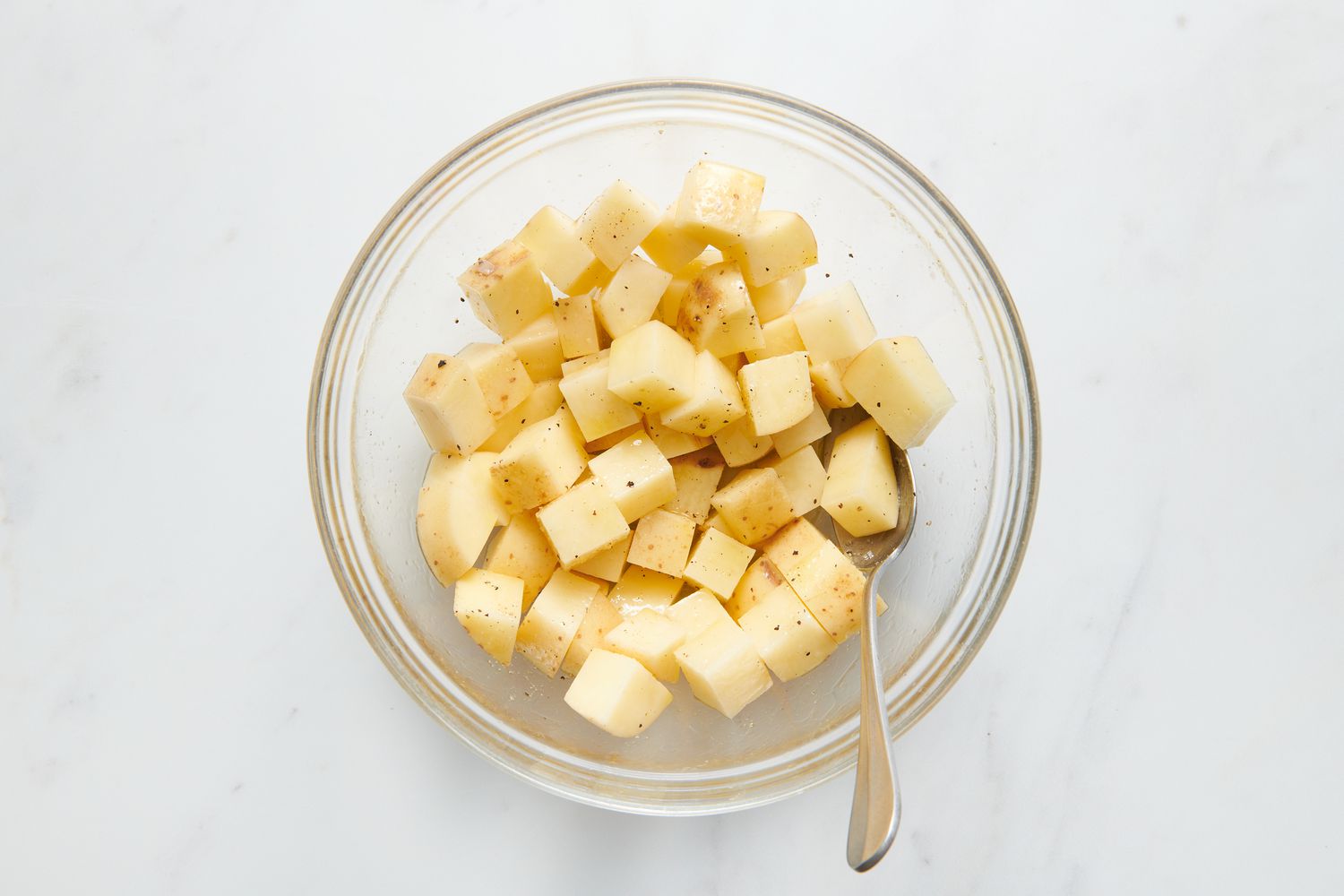 A large bowl of cubed, peeled russet potatoes tossed with olive oil, salt, and pepper