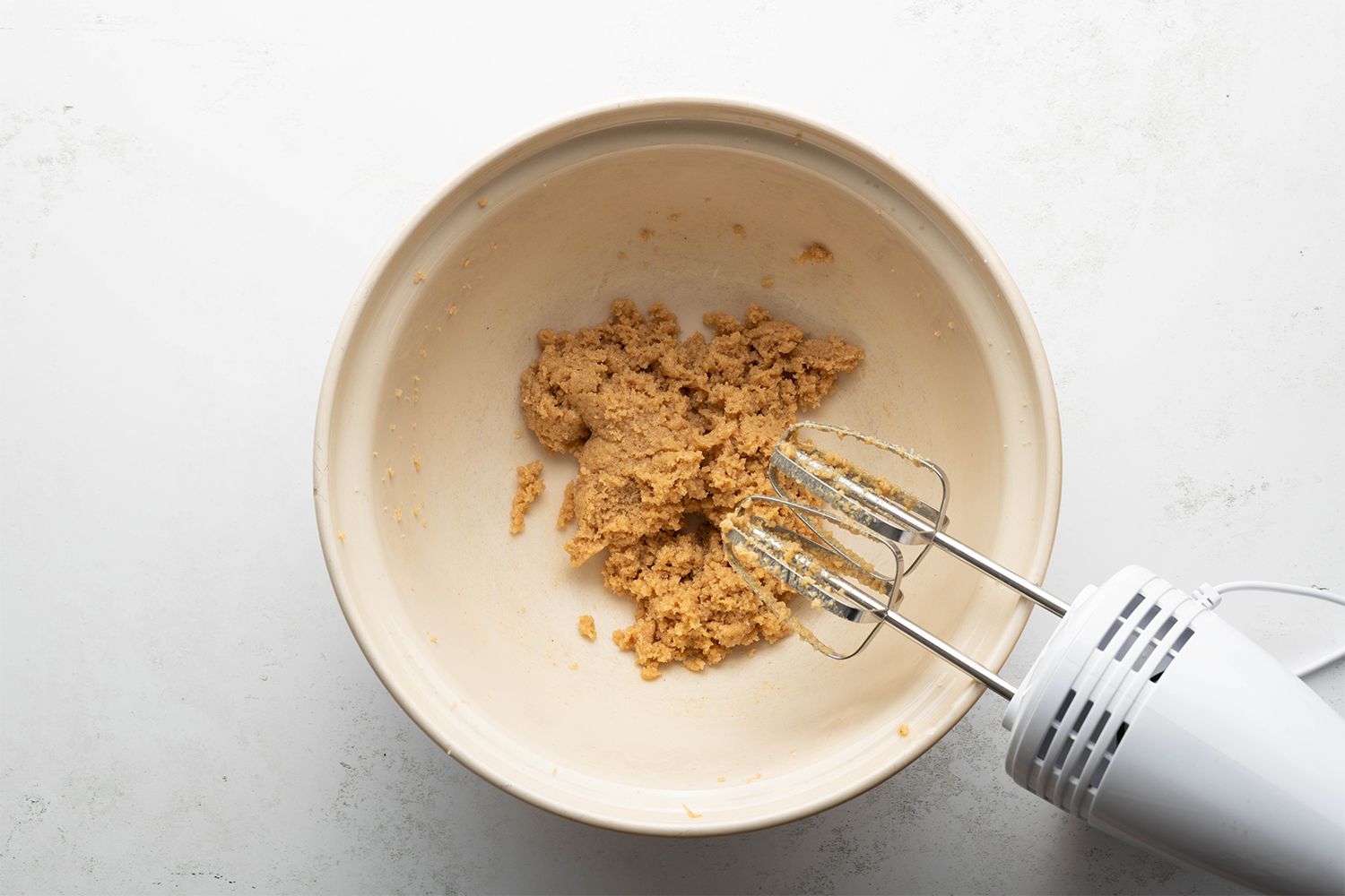 Peanut butter and sugar mixture in a bowl, next to a hand mixer 