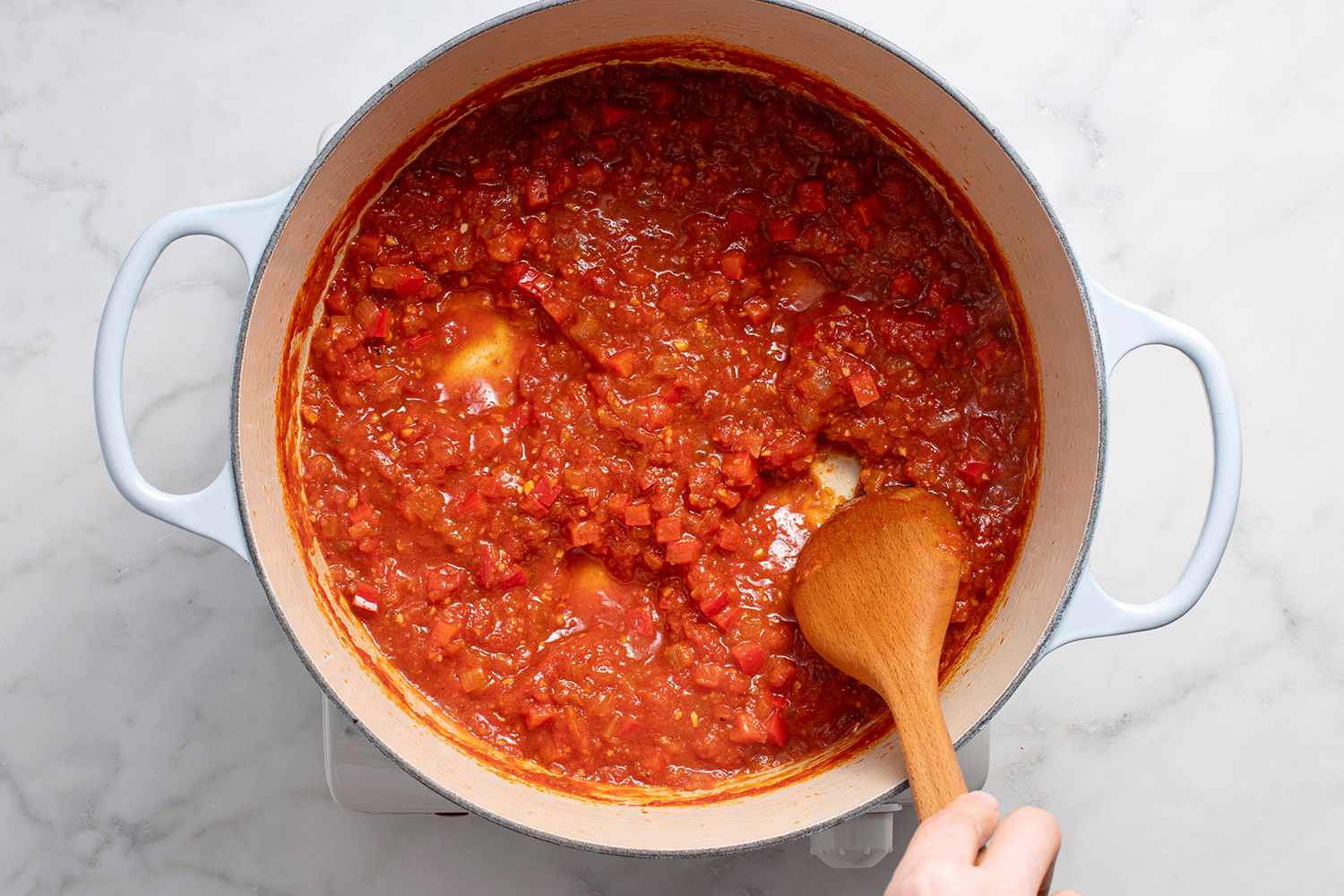 Space created in the tomato sauce in the pot, with a wooden spoon, on a burner 