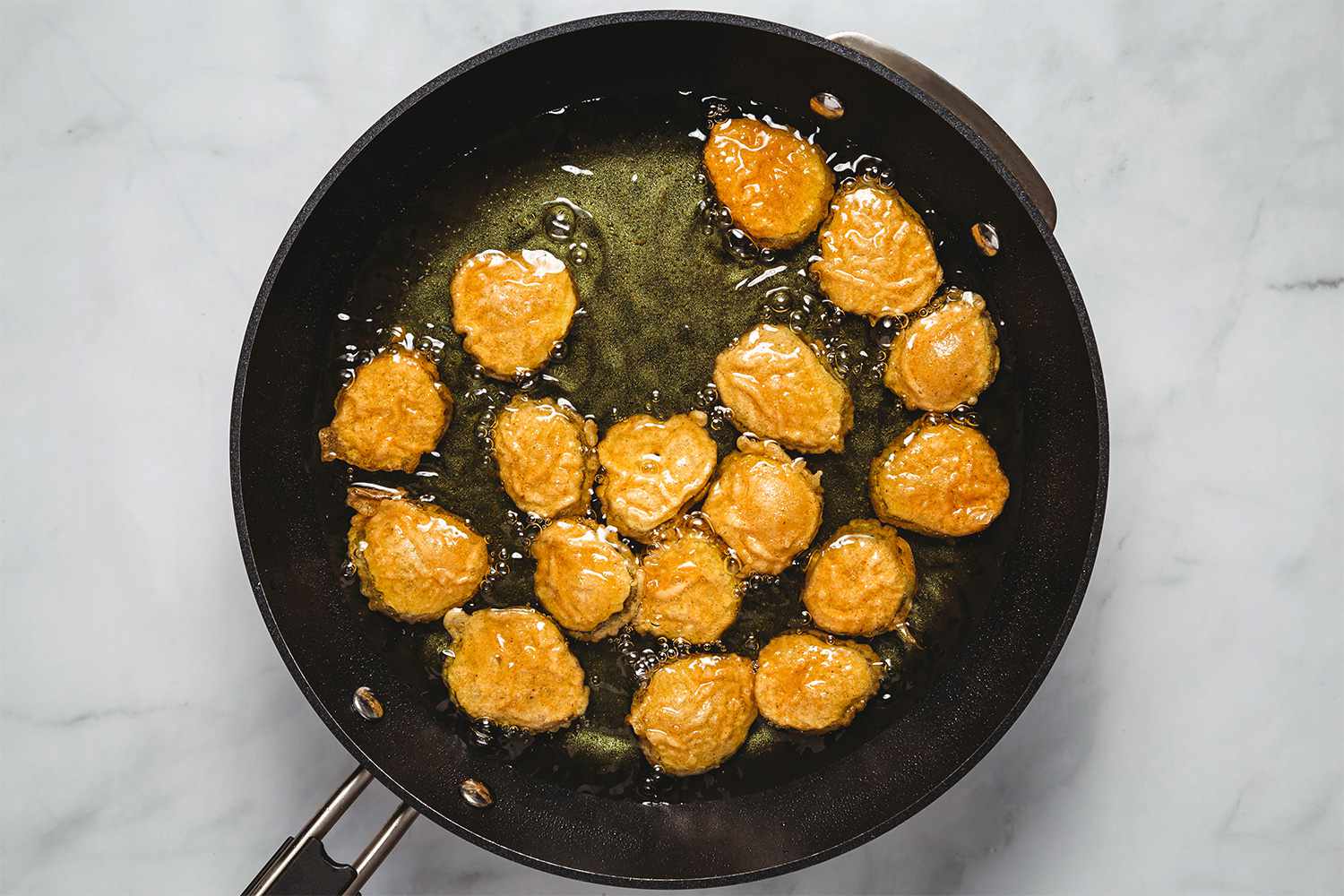 Battered pickles frying in a pan with oil 