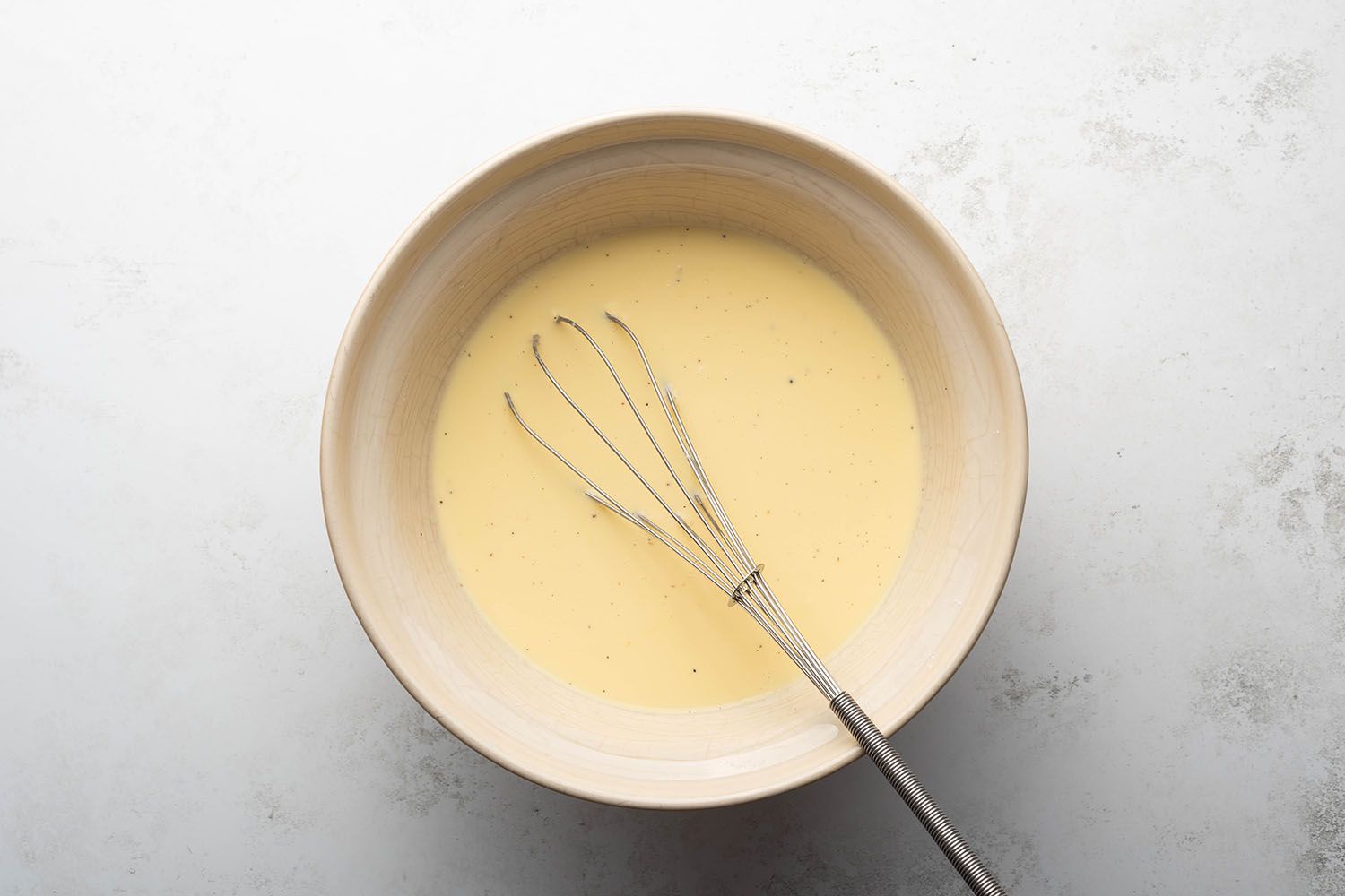 Pudding mix, vanilla bean, and milk in a large bowl in a bowl with a whisk 