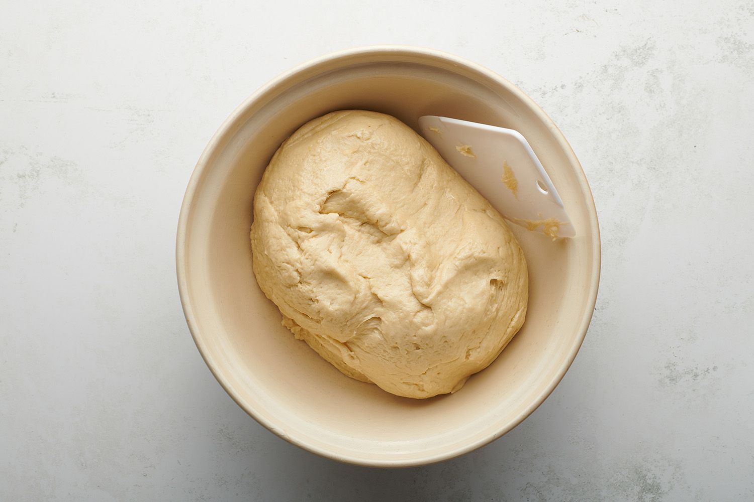 Dough in a bowl, with a dough scraper 
