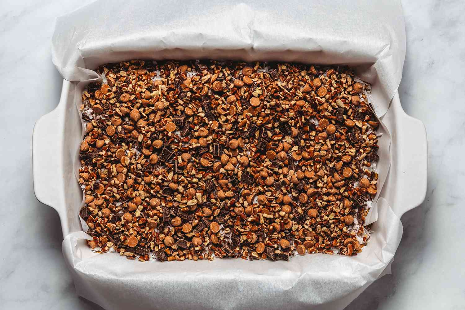 Chocolate, butterscotch, and nuts on top of the coconut flakes in the prepare baking dish