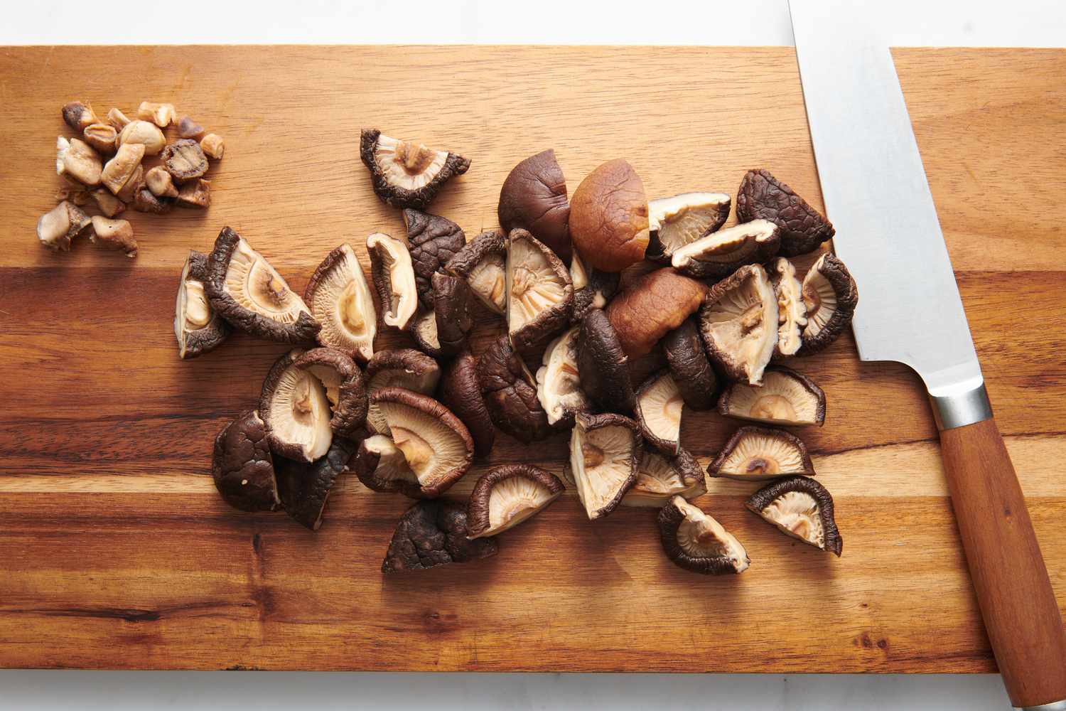 A cutting board with soaked shiitake mushrooms with the stems trimmed, cut in half